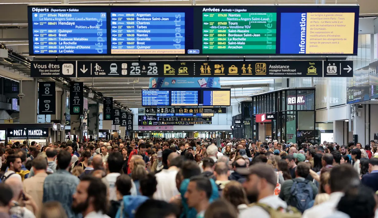 Para penumpang berkumpul di sekitar layar monitor yang menunjukkan jadwal keberangkatan dan kedatangan di stasiun kereta Gare Montparnasse di Paris pada tanggal 26 Juli 2024. (Thibaud MORITZ / AFP)