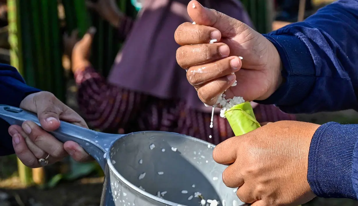 Seorang peserta mengisi tabung bambu dengan beras ketan, yang kemudian diisi dengan santan dan diletakkan di atas api unggun untuk membuat hidangan tradisional yang dikenal sebagai lemang, selama acara memasak massal di Blang Pidie, Kabupaten Aceh Barat Daya, Aceh, pada Sabtu 25 April 2026. (CHAIDEER MAHYUDDIN/AFP)