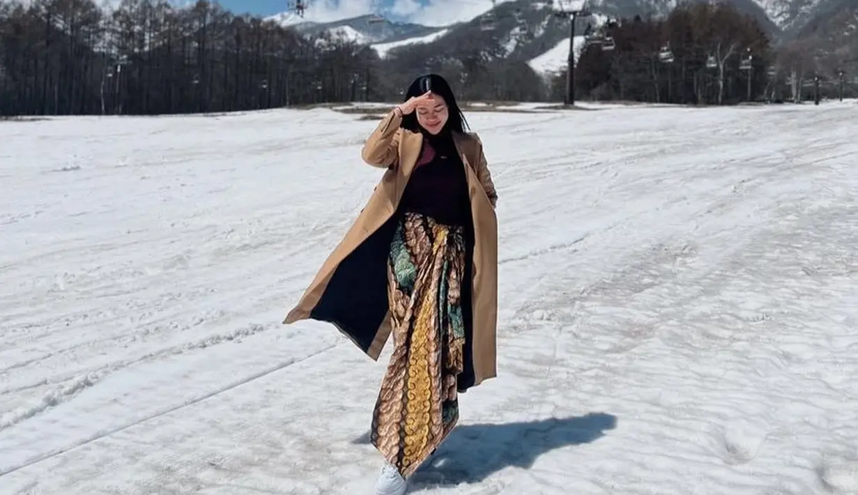Bukan kimono, Yura justru tampil kece dengan kain lilit dipadukan long coat cokelat dan innernya saat berada di tengah hamparan salju.  Credit: Instagram (@yurayunita)
