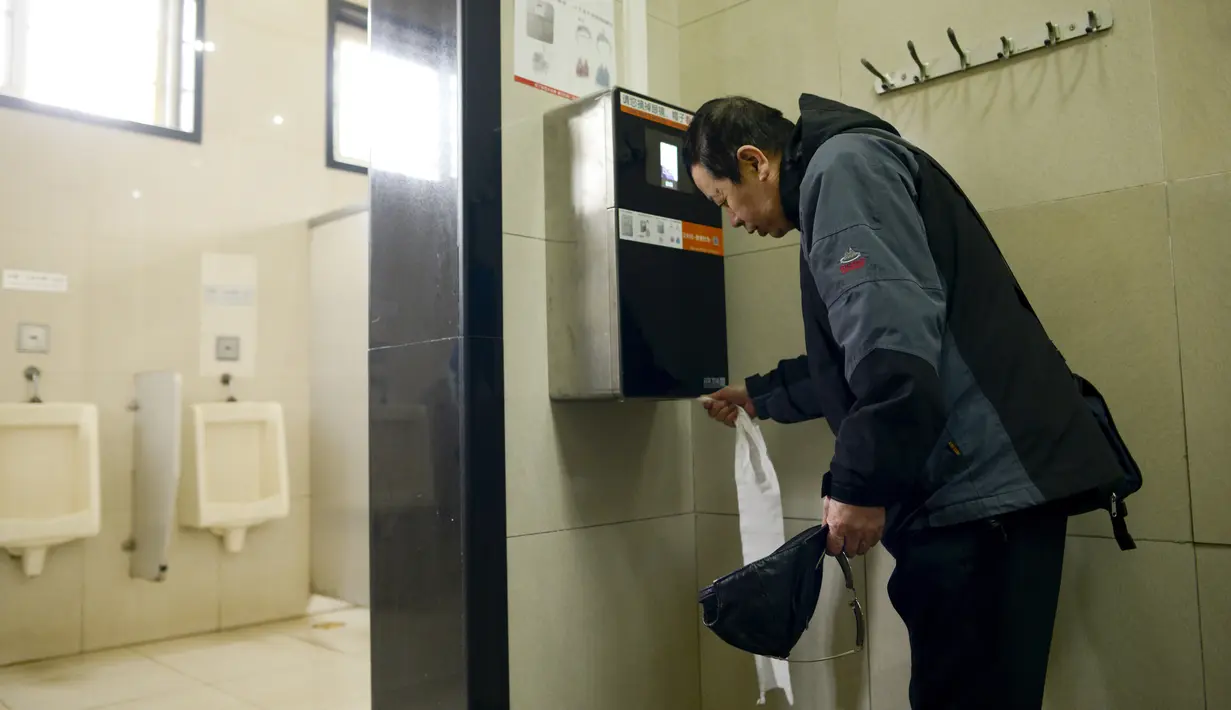 Pengunjung mengambil tisu yang dipasangi alat pendeteksi wajah di toilet umum Temple of Heaven, Beijing, China, Selasa (21/3). Pengujung toilet baru bisa mengambil tisu setelah wajahnya dipindai oleh kamera di alat ini selama tiga detik. (WANG Zhao/AFP)