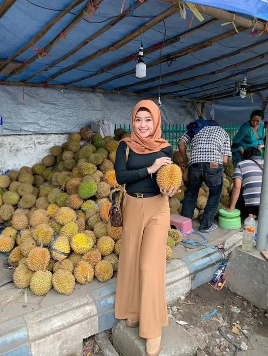 Saat berpergian, Vivi sesekali mengenakan hijab. Saat membeli durian ia memilih penampilan yang simple tapi modis. Pedangdut ini mengenakan kaos hitam yang dipadukan dengan kulot berwarna coklat muda serta hijab yang senada, cocok banget. (Liputan6.com/IG/@viviartika)