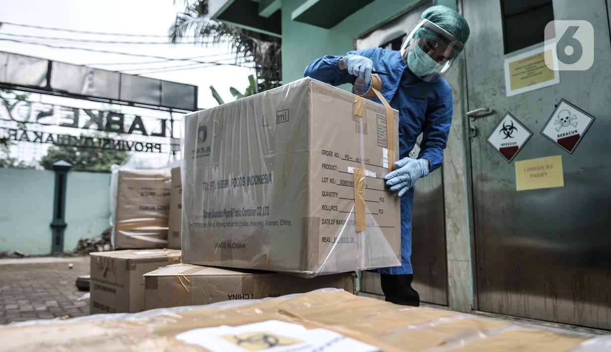 Petugas berpakaian APD mengemas limbah Covid-19 ke dalam kardus berlapis plastik di Tempat Penyimpanan Sementara Limbah B3 di Labkesda DKI Jakarta, Selasa (4/8/2020). Setiap kantong berisi limbah Covid-19 dibawa ke ruang sterilisasi sebelum diangkut ke tempat pembuangan. (merdeka.com/Iqbal Nugroho)