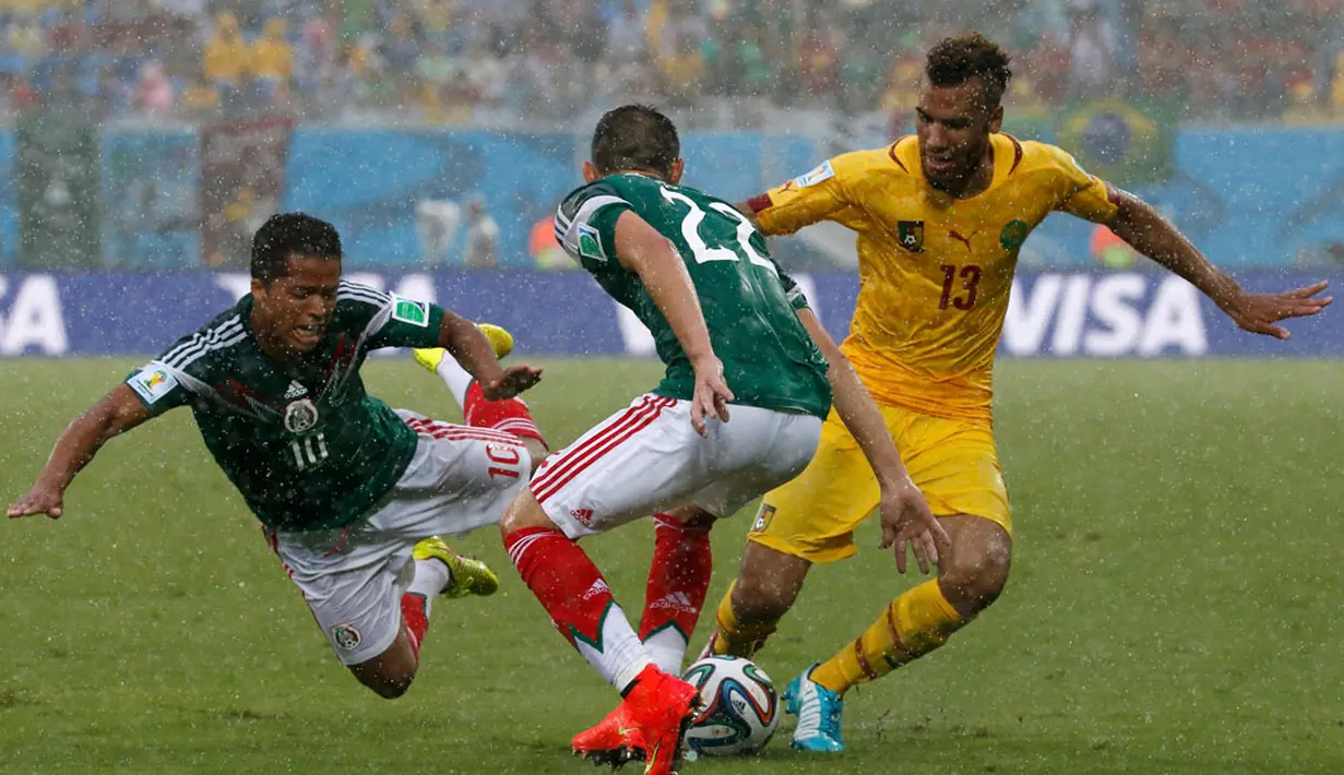 Di bawah guyuran hujan, laga Meksiko kontra Kamerun berlangsung cukup ketat. Tampak dua pemain Meksiko mencoba menghalangi pergerakan Eric-Maxim Choupo Moting (Kamerun - kiri) di Estadio das Dunas, Natal, Brasil, (13/6/2014). (REUTERS/Jorge Silva)