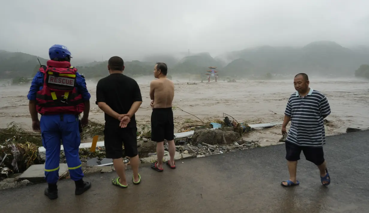 Seorang pekerja penyelamat dan warga lainnya melihat ke arah sungai yang meluap di daerah Miaofengshan di pinggiran Beijing, Selasa, 1 Agustus 2023. (AP Photo/Ng Han Guan)