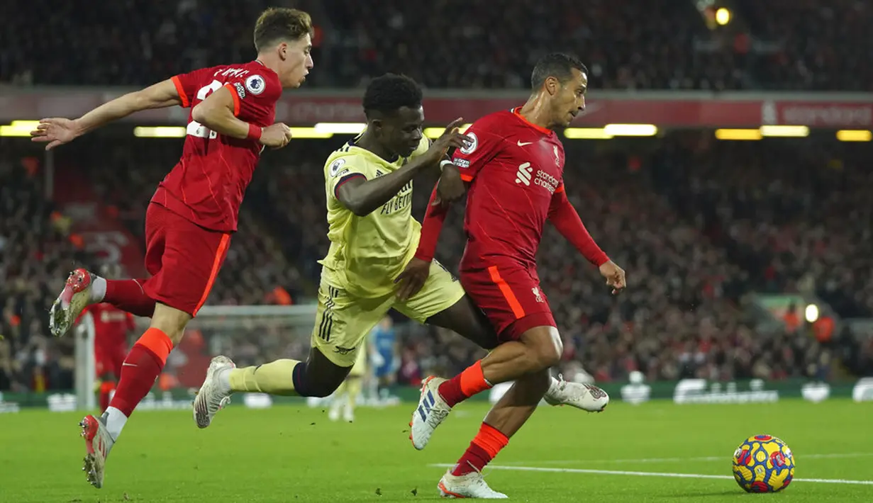 Pemain Arsenal Bukayo Saka (tengah) berebut bola dengan pemain Liverpool Kostas Tsimikas (kiri) dan Thiago pada pertandingan sepak bola Liga Inggris di Stadion Anfield, Liverpool, Inggris, 20 November 2021. Liverpool menang 4-0. (AP Photo/Jon Super)