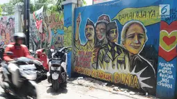 Pengendara motor melintasi mural pemilu di Jalan Karet, Depok, Jawa Barat, Rabu (20/3). Mural tersebut mengajak masyarakat untuk berpartisipasi dalam menyukseskan pemilu dengan cara damai dan menjaga meski berbeda pilihan. (Liputan6.com/Herman Zakharia)