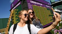 Dua wanita berselfie di sebelah papan Order of Play pada hari ketiga Kejuaraan Tenis Wimbledon 2017 di The All England Lawn Tennis Club di Wimbledon, London barat daya, Inggris (5/7). (AFP Photo/Justin Tallis)