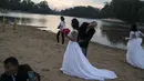 Suami dari Eliene Pereira Francisco membantu istrinya merapikan gaun setelah difoto untuk album pernikahan dengan latar belakang hutan hujan Amazon di pantai sungai Jamanxim, Brasil (2/9/2019). Mereka memutuskan untuk merayakan hari ini dengan pemotretan di tepi sungai. (Foto AP / Leo Correa)