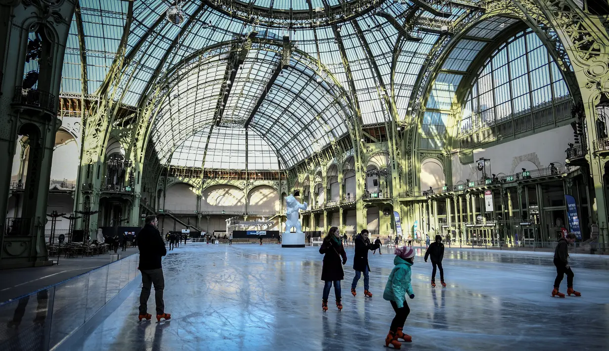 Orang-orang  berseluncur di arena ice skating di bawah kubah kaca mewah legendaris, Grand Palais, Paris, Senin (17/12). Tempat seluas 1.800 meter persegi ini menjadi arena ice skating sementara terbesar di Prancis. (STEPHANE DE SAKUTIN / AFP)
