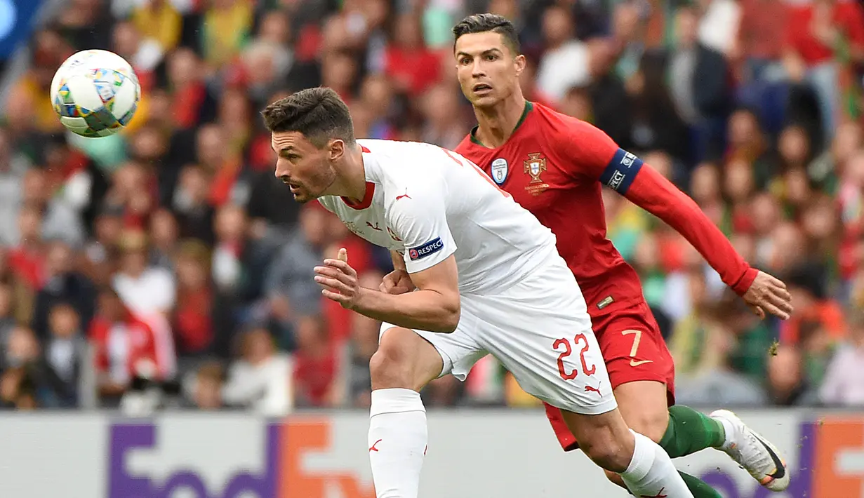 Penyerang Portugal, Cristiano Ronaldo, berebut bola dengan bek Swiss, Fabian Schar, pada laga UEFA Nations League di Estadio Do Dragao, Porto, Kamis (6/6) dini hari WIB. Portugal menang 3-1 atas Swiss. (AFP/Miguel Riopa).