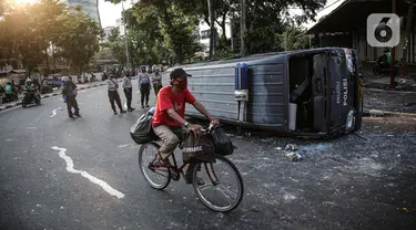 Seorang pengendara sepeda melintas dekat sebuah mobil polisi yang dirusak massa saat bentrok di kawasan Pejompongan, Jakarta, Rabu (7/10/2020). (Liputan6.com/Faizal Fanani)