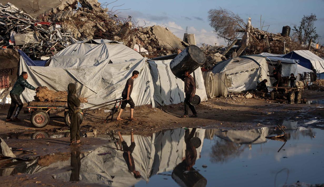 Seorang pria Palestina yang terlantar menarik gerobak setelah hujan deras di kota Jabalia, Jalur Gaza utara, pada Selasa 25 November 2025. Hujan deras yang mengguyur wilayah di Jalur Gaza, pada Selasa (25/11/2025) menyebabkan sejumlah lokasi penampungan pengungsi terendam banjir. (Omar AL-QATTAA/AFP)