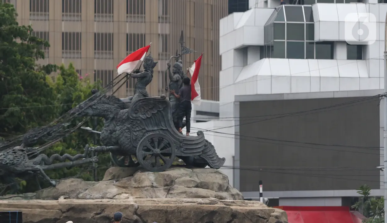 Massa aksi demo tolak omnibus law UU Cipta Kerja naik ke atas patung arjuna wiwaha membawa bendera merah putih di Jalan Medan Merdeka Barat, Jakarta Pusat, Selasa (20/10/2020). Mereka sempat mengibarkan bendera selama kurang lebih lima menit di atas patung. (Liputan6.com/Herman Zakharia)