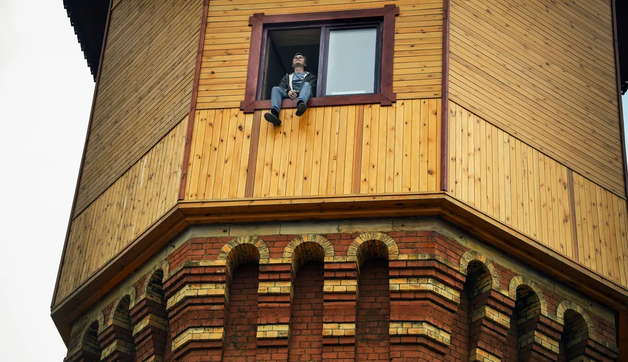 Pengusaha Rusia Alexander Lunev duduk di jendela bekas menara air, yang diubah menjadi apartemen, di kota Tomsk, Siberia pada 7 September 2020. Alexander Lunev mulai membangun kembali menara air yang dibuat pada 1895 tersebut, menjadi sebuah apartemen untuk dirinya. (Alexander NEMENOV / AFP)