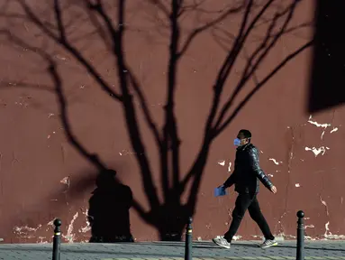Seorang warga yang mengenakan masker berjalan dekat bayang-bayang pohon di Beijing, China, 27 Desember 2022. Perusahaan menyambut baik keputusan China untuk mengakhiri karantina bagi pelancong dari luar negeri sebagai langkah penting untuk menghidupkan kembali aktivitas bisnis yang merosot, sementara Jepang mengumumkan pembatasan pengunjung saat infeksi melonjak. (AP Photo/Ng Han Guan)