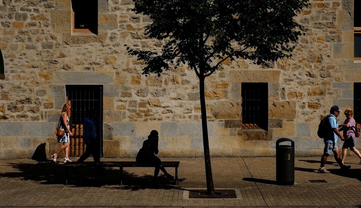 Seorang wanita berteduh di bawah pohon sambil menunggu bus saat musim panas, di Pamplona, Spanyol utara, (3/8). Dua orang tewas akibat sengatan panas di Spanyol ketika Eropa dilanda gelombang panas. (AP Photo/Alvaro Barrientos)