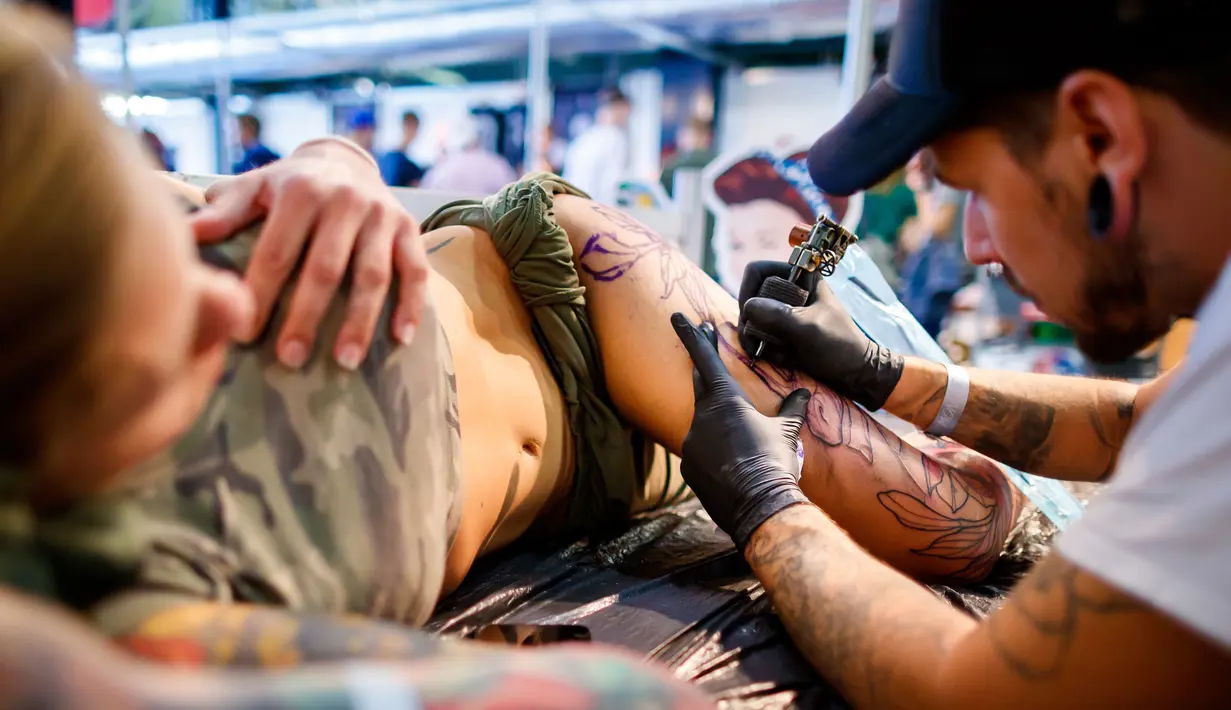 Seorang seniman mentato badan pengunjung wanita dalam acara edisi keempat Montreux Tattoo Convention di Montreux, Swiss  (22/9). Lebih 150 seniman tato dari 22 negara berkumpul dalam acara tersebut. (Valentin Flauraud/Keystone via AP)