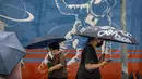 Para komuter yang mengenakan masker dan membawa payung berjalan melewati mural seorang astronot saat hujan di kawasan pusat bisnis di Beijing, China, 12 Juli 2022. Beijing telah membatalkan rencana untuk mengizinkan hanya orang yang divaksinasi yang memasuki ruang publik. (AP Photo/Mark Schiefelbein)