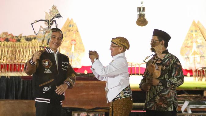 Presiden Joko Widodo (Jokowi) memainkan wayang kulit disaksikan dalang Ki Mantep Sudarsono (tengah) dalam Pagelaran Wayang Kulit 74 Tahun Indonesia Merdeka di halaman depan Istana Merdeka, Jakarta, Jumat (2/8/2019). Pagelaran wayang mengangkat tema 