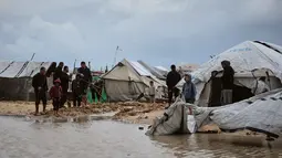 Hujan deras dan angin kencang merendam tenda-tenda para pengungsi, dan memperburuk krisis kemanusiaan yang sudah ada. Tampak dalam foto, warga Palestina berjalan melewati area yang tergenang banjir di kamp tenda sementara setelah hujan lebat di Kota Gaza, Kamis, 26 Maret 2026 (AP Photo/Jehad Alshrafi)