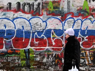 Seorang perempuan berjalan melewati grafiti bertuliskan "Rusia" dengan warna bendera tiga warna Rusia di "Tembok Tsoi" di pusat kota Moskow pada 7 Desember 2023. (NATALIA KOLESNIKOVA/AFP)