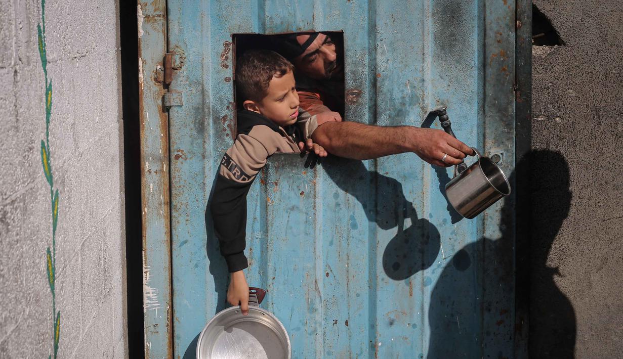 Warga Palestina yang terlantar, anak-anak, dan dewasa, menunggu makanan di sebuah tempat penampungan yang telah dihuni keluarga-keluarga di Nuseirat, pusat Jalur Gaza, pada 23 November 2025. Badan kemanusiaan Perserikatan Bangsa Bangsa (PBB) untuk Koordinasi Urusan Kemanusiaan (OCHA) mengatakan pada Sabtu 22 November 2025 bahwa peningkatan bantuan untuk Gaza masih terhambat. (EYAD BABA/AFP)