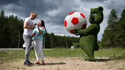 Pasangan berada di dekat patung seekor anak beruang memegang bola yang terbuat dari dedaunan di dekat bandara Samara, Rusia (11/6). Rusia akan menjadi tuan rumah turnamen sepak bola Piala Dunia 2018. (AFP Photo/Fabrice Coffrini)