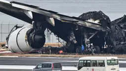Para petugas melihat puing-puing pesawat penumpang Japan Airlines (JAL) yang terbakar di landasan pacu di Bandara Internasional Tokyo di Haneda di Tokyo pada tanggal 3 Januari 2024. (Richard A. Brooks/AFP)