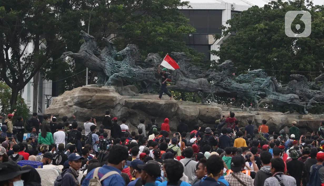 Massa aksi demo tolak omnibus law UU Cipta Kerja naik ke atas patung arjuna wiwaha mengibarkan bendera merah putih di Jalan Medan Merdeka Barat, Jakarta Pusat, Selasa (20/10/2020). Mereka sempat mengibarkan bendera selama kurang lebih lima menit di atas patung. (Liputan6.com/Herman Zakharia)