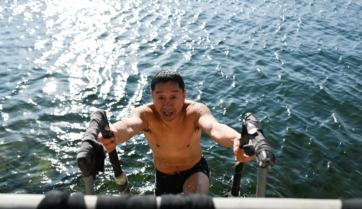 Seorang pria muncul setelah berenang di sebuah danau yang airnya sebagian membeku di Beijing pada Senin (30/12/2019). Penduduk lokal banyak menggemari kebiasaan berenang di musim dingin dimana banyak sungai dan danau-danau mulai membeku. (WANG ZHAO / AFP)