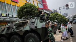 Dua siswa berjalan dekat  Prajurit TNI dan  satu unit kendaraan Anoa di kawasan LTC Glodok, Jakarta, Jumat (18/10/2019). Penjagaan tersebut guna memberikan rasa aman bagi masyarakat menjelang pelantikan presiden dan wakil presiden terpilih, 20 Oktober 2019. (Liputan6.com/Faizal Fanani)