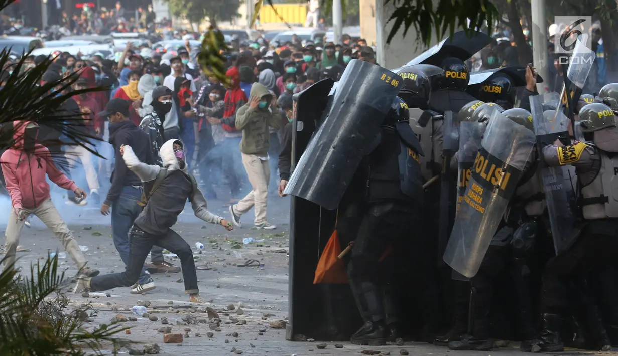 Massa melempar batu ke arah polisi yang membentuk barikade dengan tameng di sekitaran Gedung DPR RI, Jakarta, Senin (30/9/2019). Kericuhan pecah lantaran massa yang kebayakan terdiri dari pelajar tersebut berusaha masuk ke area depan DPR. (Liputan6.com/Angga Yuniar)