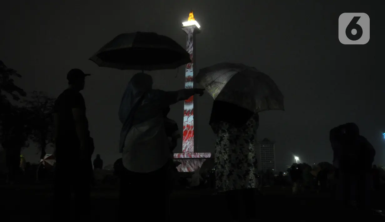 Pengunjung menyaksikan penampilan video mapping saat malam pergantian tahun di kawasan Monumen Nasional, Jakarta, Selasa (31/12/2019). Meski Jakarta diguyur hujan sejak Selasa (31/12) sore, warga tetap mendatangi kawasan Monas untuk merayakan malam pergantian tahun. (Liputan6.com/Helmi Fithriansyah)