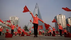 Kelompok Serikat Wanita Sosialis mengibarkan bendera saat melakukan propaganda di depan Hotel Ryugyong, Pyongyang, Korea Utara, Sabtu (9/3). Mereka mengibar-ngibarkan bendera sambil menyanyikan lagu-lagu patriotik selama jam sibuk. (Ed Jones/AFP)