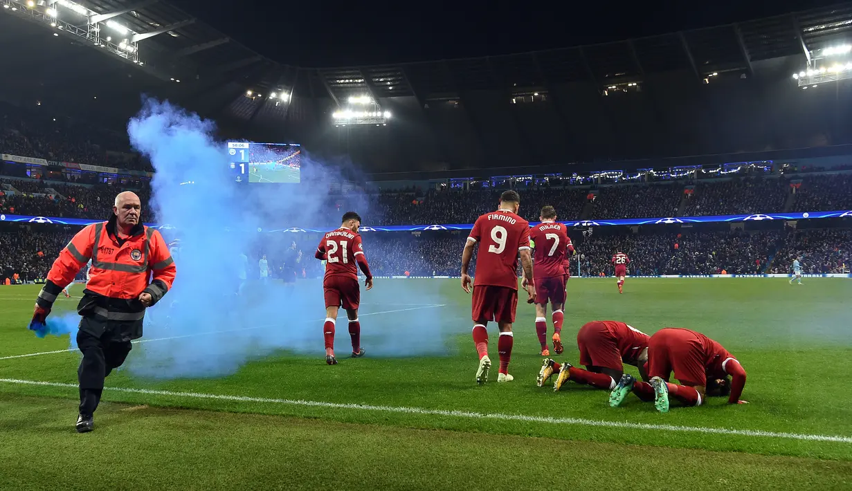 Seorang petugas mengambil flare saat pemain Liverpool Mohamed Salah bersama rekannya Sadio Mane melakukan selebrasi dalam pertandingan Liga Champions di Etihad Stadium (10/4). Salah menyumbang satu gol untuk Liverpool. (AFP/Paul Ellis)