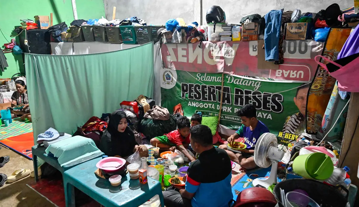 Warga pun terpaksa terus menetap dan beraktivitas di tenda-tenda penampungan dengan fasilitas seadanya yang dinilai kurang layak untuk ditinggali dalam jangka waktu lama. Tampak dalam foto, sebuah keluarga berbuka puasa Ramadan di tempat penampungan sementara bagi korban banjir di Meurah Dua, Kabupaten Pidie Jaya, Provinsi Aceh, pada 21 Februari 2026, setelah banjir dan tanah longsor dahsyat melanda Sumatra, akhir November 2025 lalu. (CHAIDEER MAHYUDDIN/AFP)