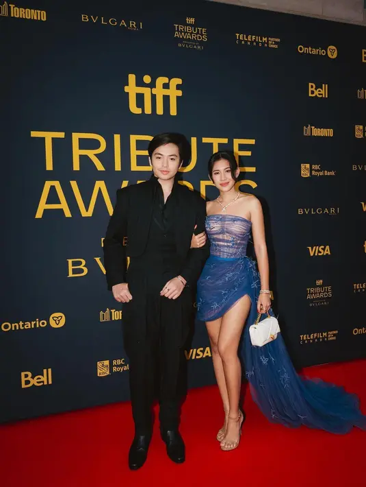 Couple yang satu ini tak perlu diragukan lagi gayanya. Shenina Cinnamon tampil cantik dengan dress biru tanpa tali dan mini, diberi pemanis detail train panjang yang mencapai lantai. Sedangkan Angga Yunanda tampil serba hitam dengan jas dan celana, serta kemeja. [Foto: Instagram/shenacinnamon]