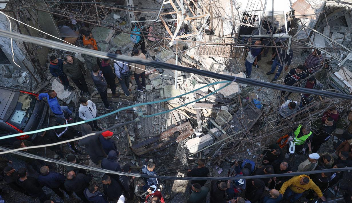 Orang-orang berkumpul di sekitar bangunan yang dirusak dan dibakar oleh pasukan Israel selama penggerebekan di kamp pengungsi Jenin Tepi Barat, pada 26 Januari 2023. Serangan Israel di kamp pengungsi Jenin hari ini menewaskan 9 warga Palestina termasuk seorang wanita lanjut usia, kata pejabat Palestina. (AFP/Jaafar Ashtiyeh)