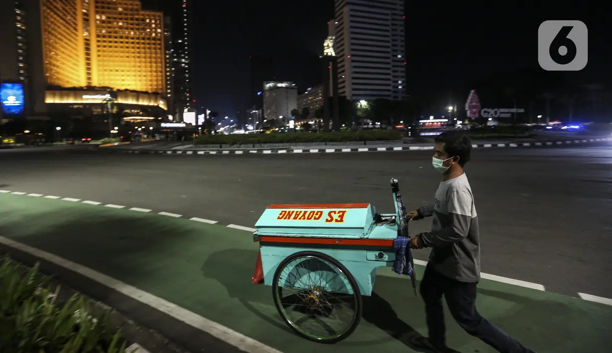 Pedagang es goyang melintas saat berlangsungnya Crowd Free Night di kawasan Bundaran HI, Jakarta, Jumat (31/12/2021). Polda Metro Jaya memberlakukan pengendalian mobilitas Crowd Free Night pada malam Tahun Baru 2022 yang berlangsung mulai pukul 22.00-04.00 WIB. (Liputan6.com/Johan Tallo)