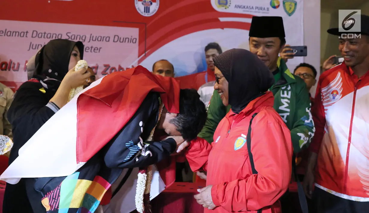 Pelari muda Indonesia, Lalu Muhammad Zohri (kiri) mencium tangan pelatih pelatnas, Eni Nuraini saat penyambutan di Terminal 3 Bandara Soetta, Tangerang, Selasa (17/7). Lalu M Zohri meraih emas lari 100m putra U-20 IAAF. (Liputan6.com/Helmi Fithriansyah)