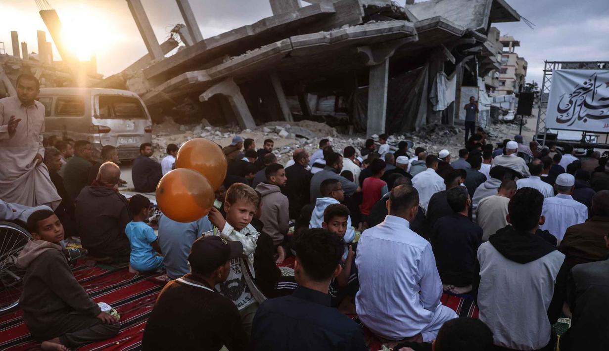 Seorang anak laki-laki memegang balon berdiri di antara warga Palestina yang berkumpul di jalan yang rusak parah untuk melaksanakan salat menandai dimulainya Idul Adha, Hari Raya Kurban, di Khan Yunis, Jalur Gaza Selatan, pada Rabu 27 Mei 2026. (BASHAR TALEB/AFP)