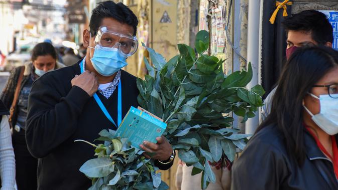 Seorang pria yang mengenakan masker membawa seikat ramuan obat tradisional yang digunakan untuk pengobatan penyakit pernapasan di Cochabamba, Bolivia pada 25 Juli 2020. Kasus infeksi virus corona dan kematian akibat COVID-19 semakin meningkat di negara Amerika Selatan tersebut. (AP Photo/Dico Solis)