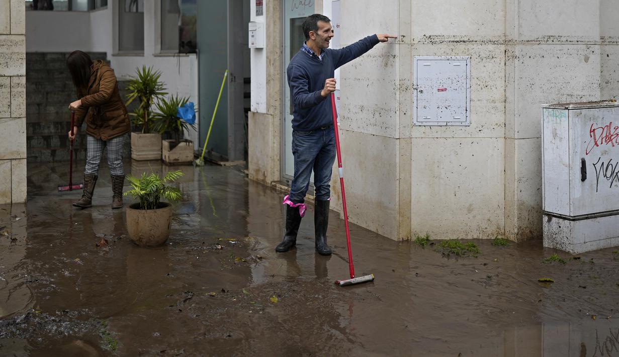 Seorang pria yang menyapu air dari sebuah gedung menunjukkan ketinggian yang dicapai air saat jalan dibanjiri semalaman di Alges, tepat di luar Lisbon, Selasa (13/12/2022). Badai Atlantik menghantam semenanjung Iberia, meninggalkan jejak kehancuran pada Selasa, terutama di Ibu kota Portugal,  Lisbon, sebelum pindah ke timur ke Spanyol.  (AP Photo/Armando Franca)