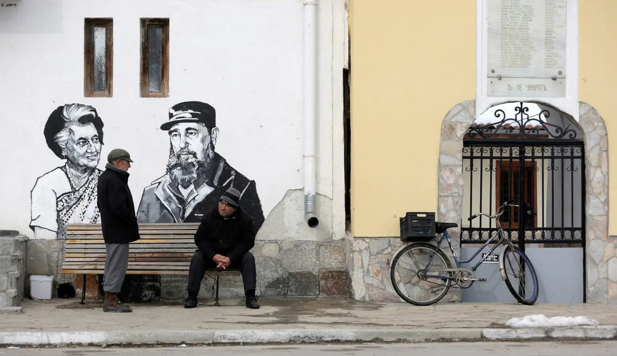 Warga setempat berbincang dekat mural yang menggambarkan Pemimpin revolusi Kuba Fidel Castro dan Perdana Menteri (PM) pertama India, Indira Gandhi di dinding sebuah bangunan di desa Staro Zhelezare, Bulgaria, Kamis (27/7). (AP Photo/Valentina Petrova)