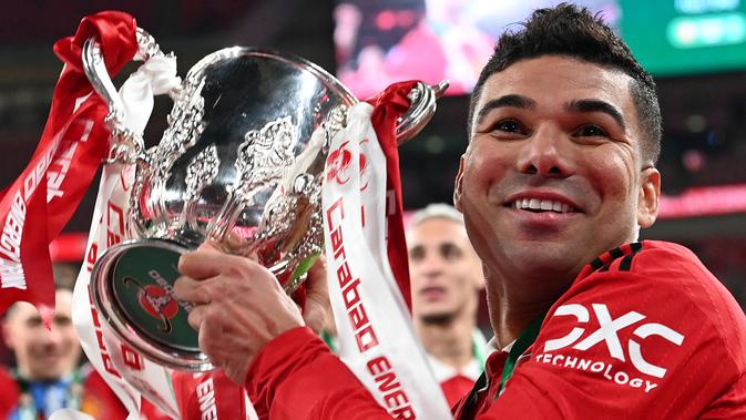 Pemain Manchester United, Casemiro mengangkat trofi setelah memenangkan final Carabao Cup 2023 melawan Newcastle United yang berlangsung di Wembley Stadium, Minggu (26/2/2023) waktu setempat. Casemiro mencetak gol pertama dalam pertandingan ini. (AFP/Adrian Dennis)