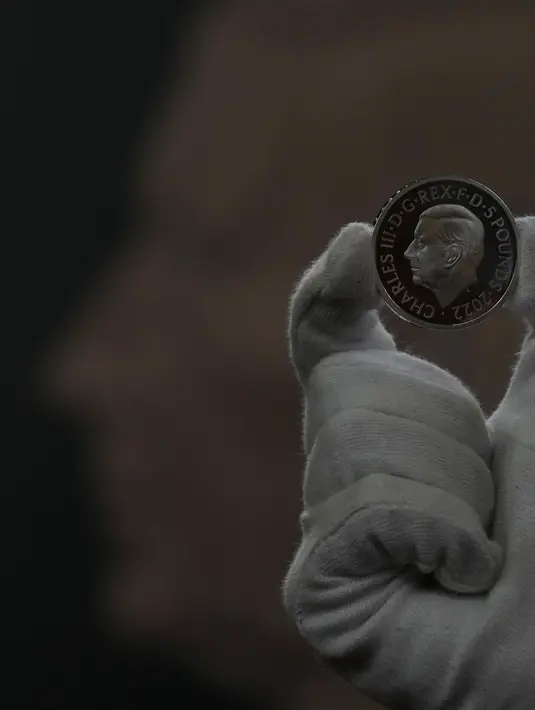 Seorang staf dari Royal Mint mengangkat koin lima pound bergambar Raja Charles III, yang akan menjadi salah satu koin pertama yang menyandang kepala raja baru, selama pratinjau pers di London, Kamis, 29 September 2022. Gambar itu dikelilingi oleh prasasti Latin yang diterjemahkan sebagai "Raja Charles III, oleh Rahmat Tuhan, Pembela Iman". (AP Photo/Alastair Grant)