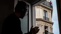 Seorang pria dan wanita bertepuk tangan saat DJ Knighthood memainkan musik dari jendela apartemennya selama lockdown di Paris, Prancis (3/4/2020). DJ Knighthood beraksi menghibur tetangga yang berdiam diri di rumah sebagai upaya mencegah penyebaran virus corona Covid-19. (AFP/Philippe Lopez)