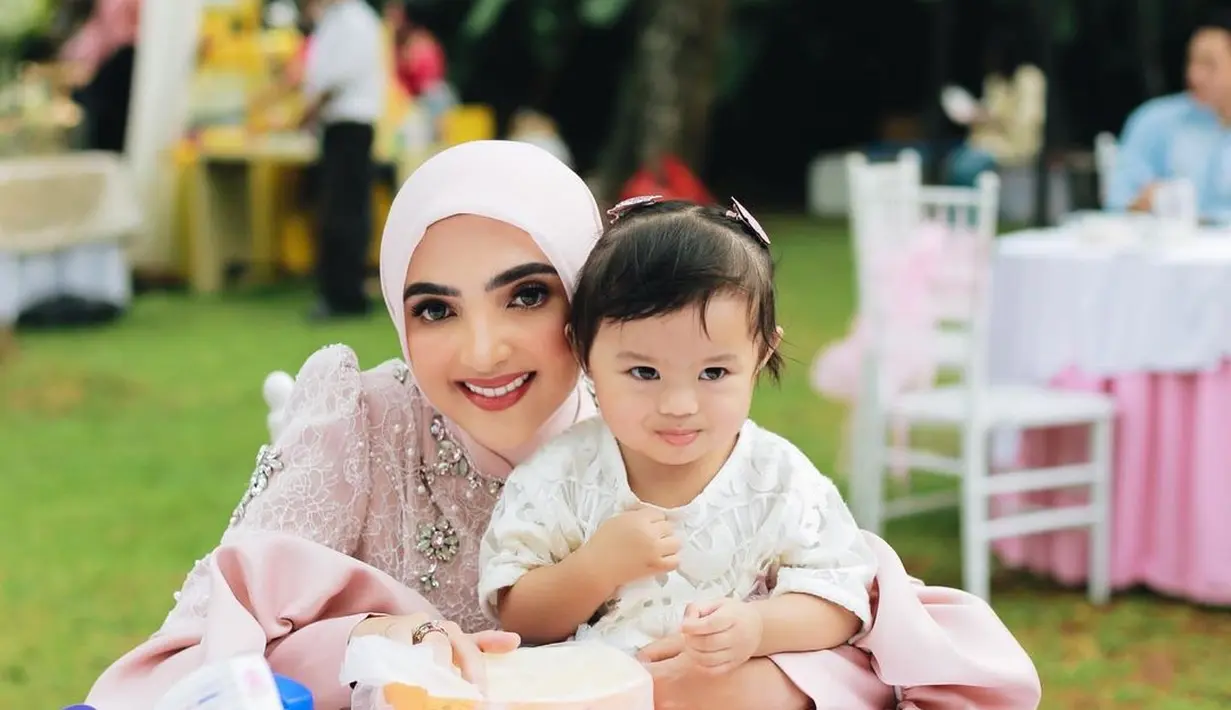 Lagi, potret gemas Ashanty bersama Ameena. Ameena didudukkan di atas meja, dengan Ashanty memeluknya dari belakang dengan outfit berwarna merah muda yang super cantik. [Foto: Instagram/ashanty_ash]