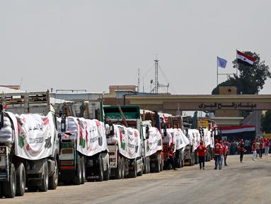 Orang-orang berjalan melewati truk-truk yang dimuat dengan bantuan untuk Gaza, menunggu di sisi Mesir dari pos perbatasan Rafah pada 18 Agustus 2025. (Khaled DESOUKI/AFP)