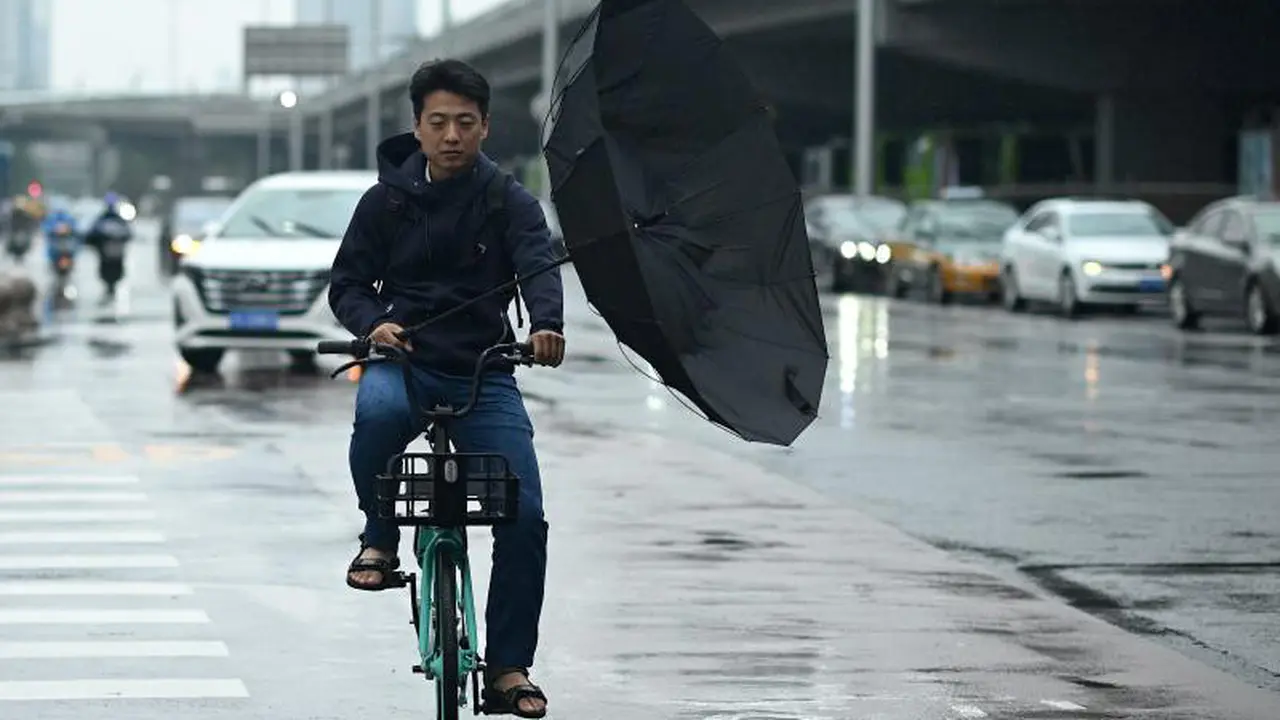 Seorang pria memegang payung sembari menggayuh pedal sepeda di tengah badai yang menghantam Beijing, China pada Senin (12/7) (AFP)